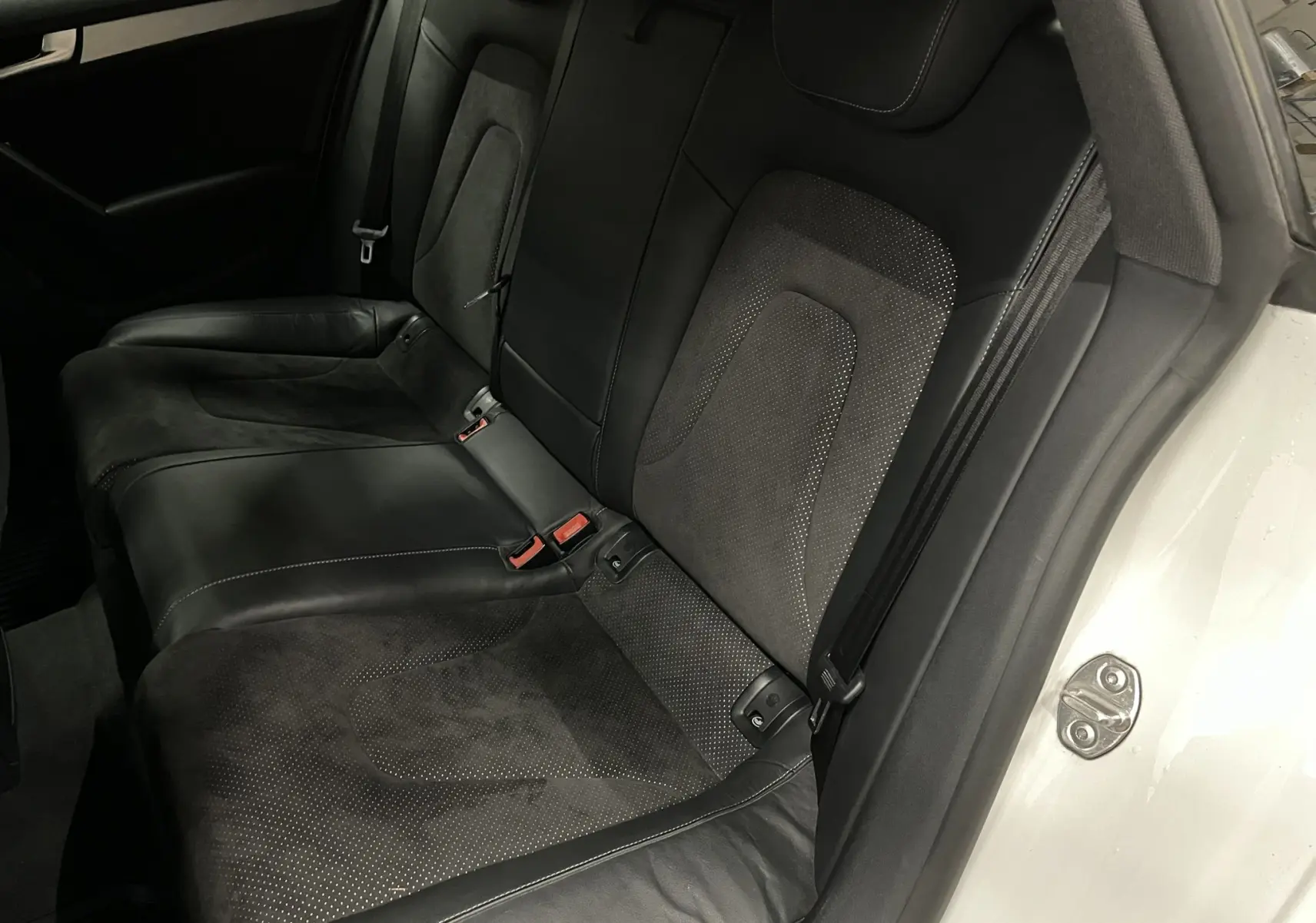 Vue intérieure des sièges arrière noirs en cuir et alcantara de l'Audi A5 Sportback blanche, porte arrière ouverte.