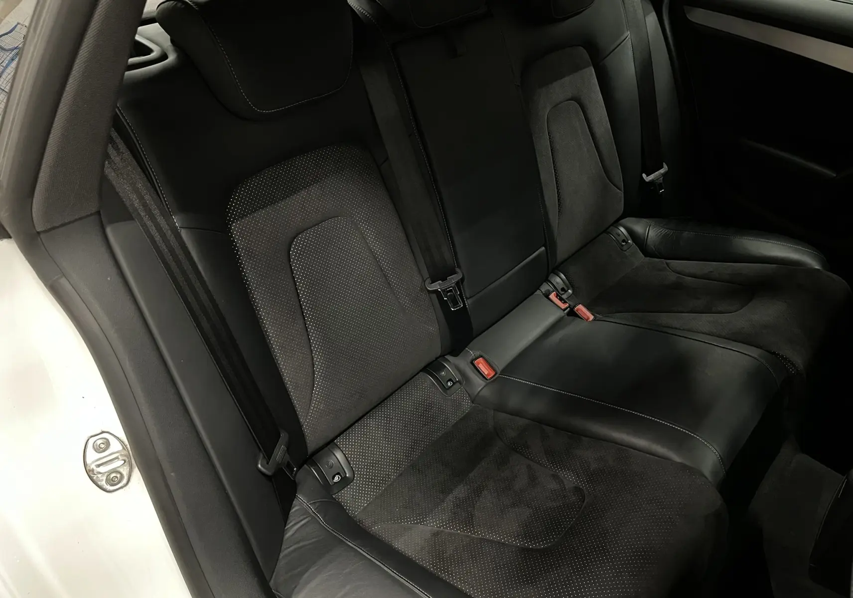 Vue intérieure de la banquette arrière noire en cuir et alcantara de l'Audi A5 Sportback blanche, côté gauche ouvert.