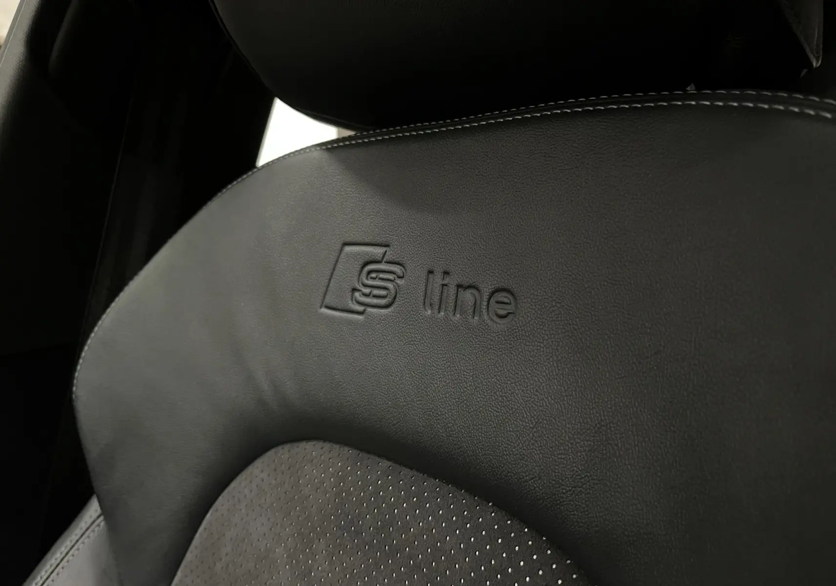 Gros plan sur le siège avant noir en cuir et alcantara avec logo S line embossé dans une Audi A5 Sportback blanche.