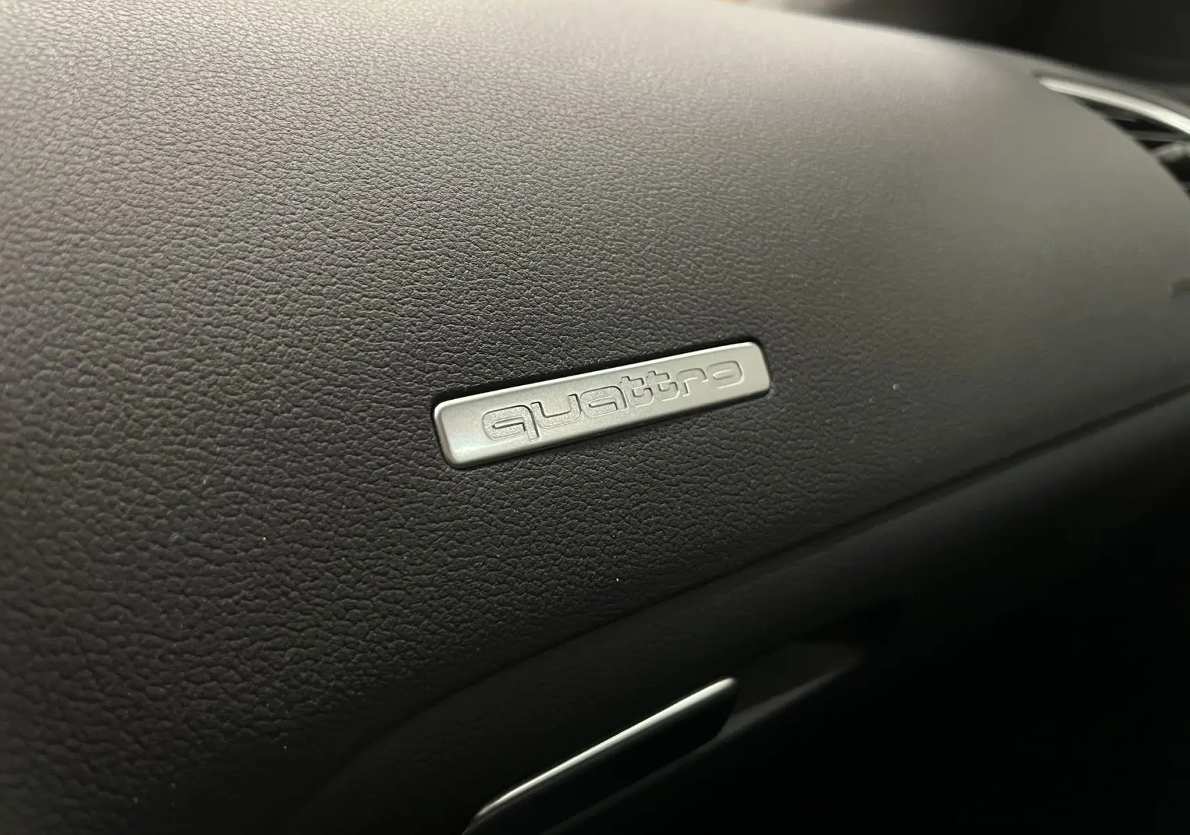 Gros plan sur le badge Quattro argenté sur le tableau de bord noir de l'Audi A5 Sportback blanc.