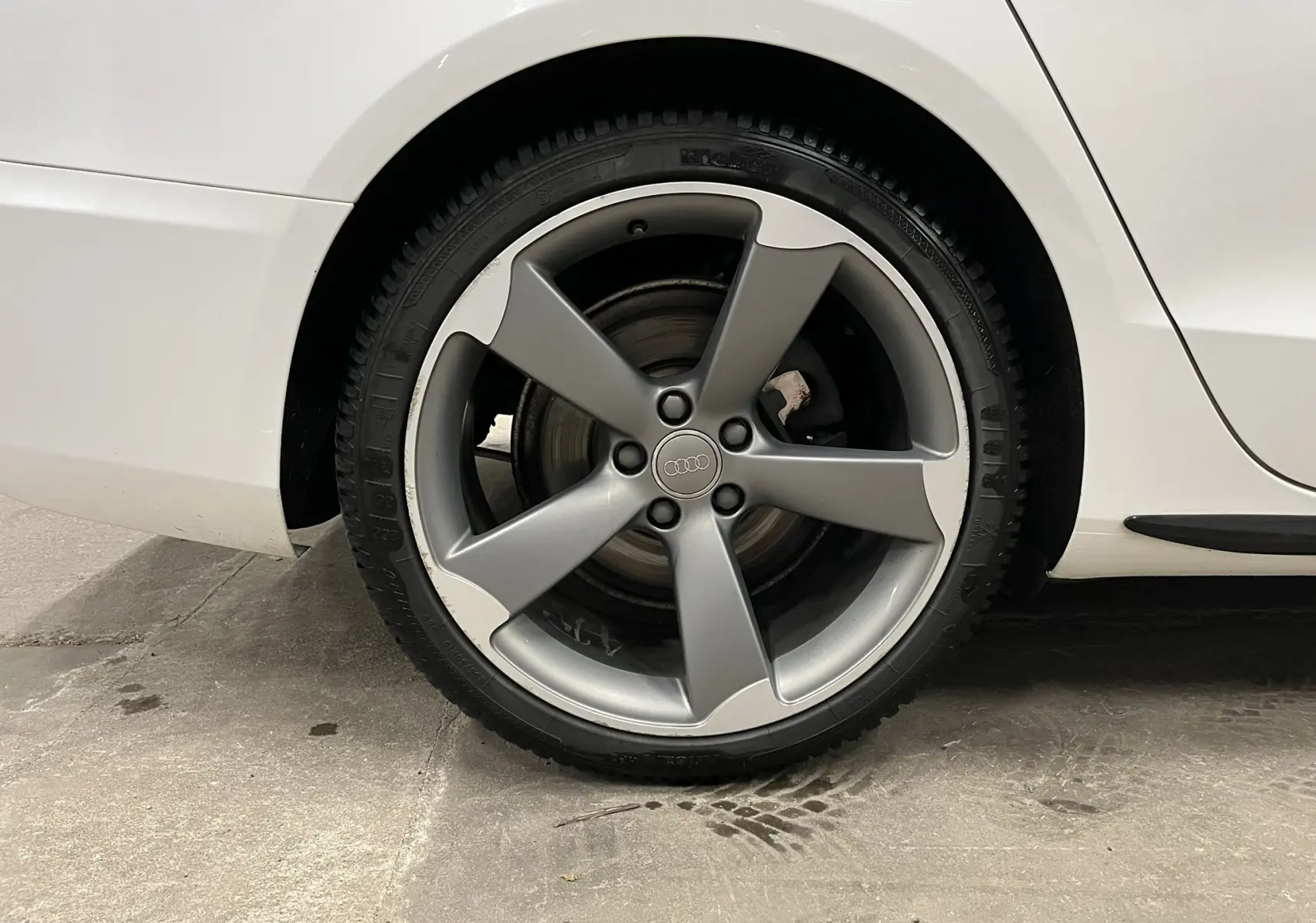 Gros plan sur la roue arrière droite de l'Audi A5 Sportback blanche avec jante alliage grise à cinq branches.