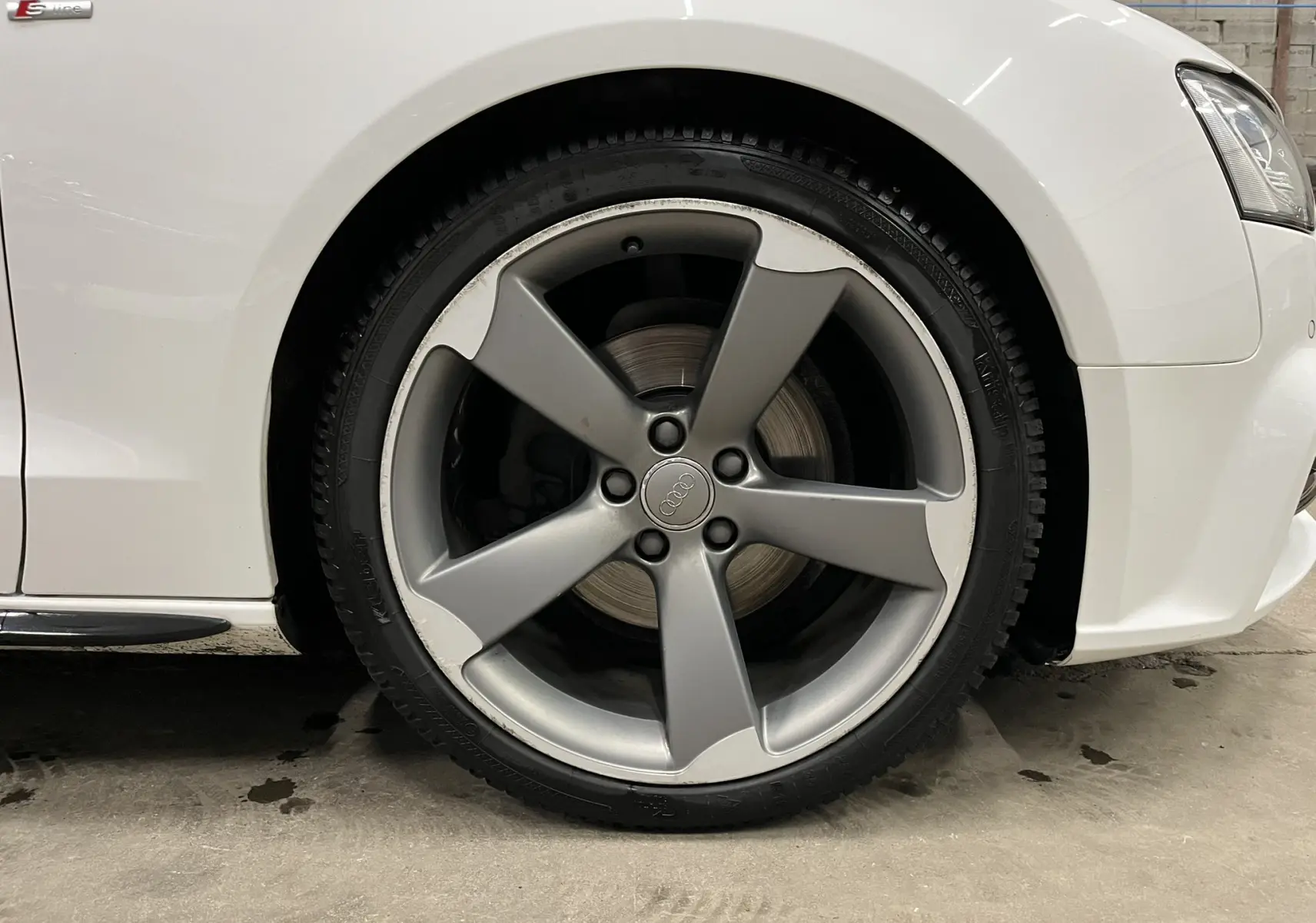 Gros plan sur la roue avant droite de l'Audi A5 Sportback blanche avec jante alliage cinq branches et logo Audi au centre.