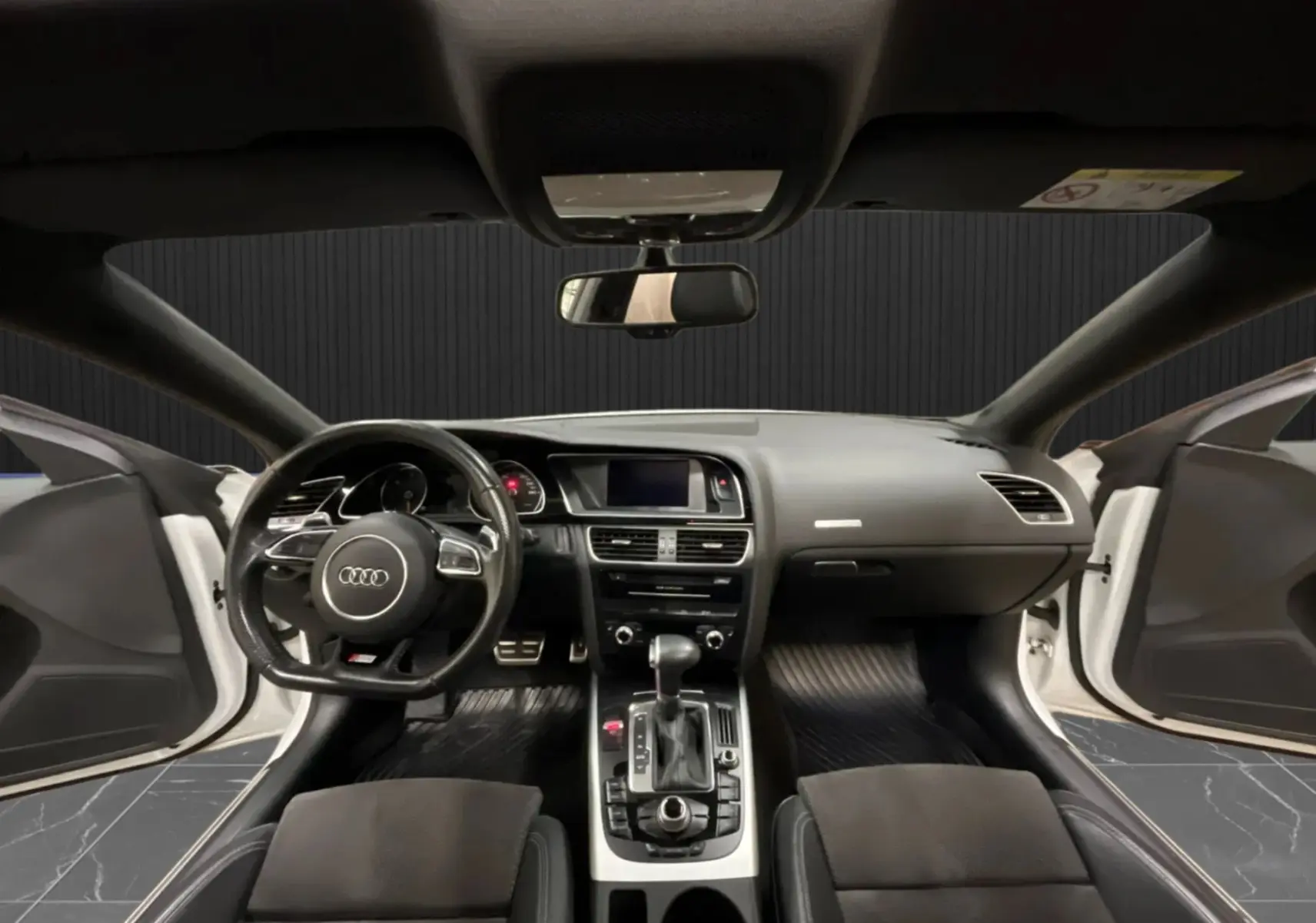 Vue intérieure avant de l'Audi A5 Sportback blanche 2015, tableau de bord et volant avec portes ouvertes.