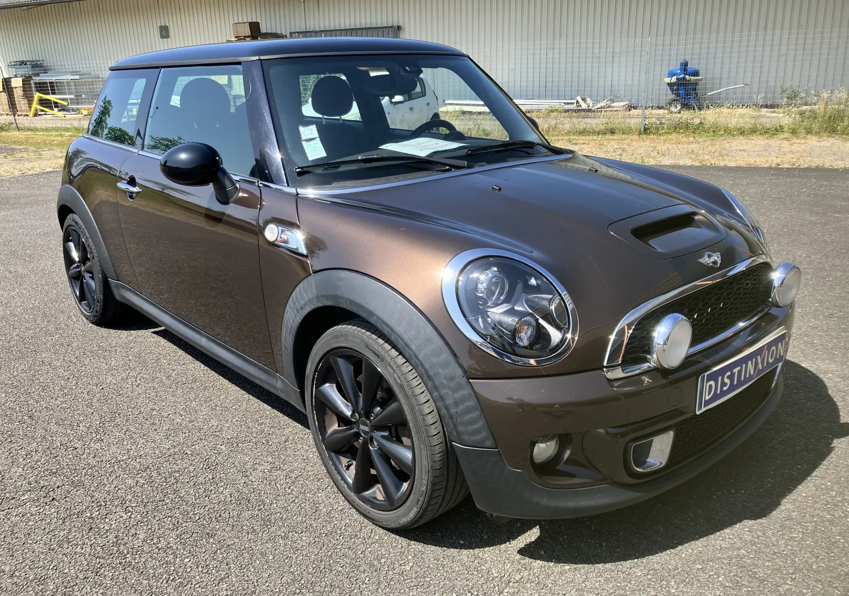 MINI Cooper S R56 marron vue 3/4 avant droit avec phares additionnels et jantes noires sur parking.