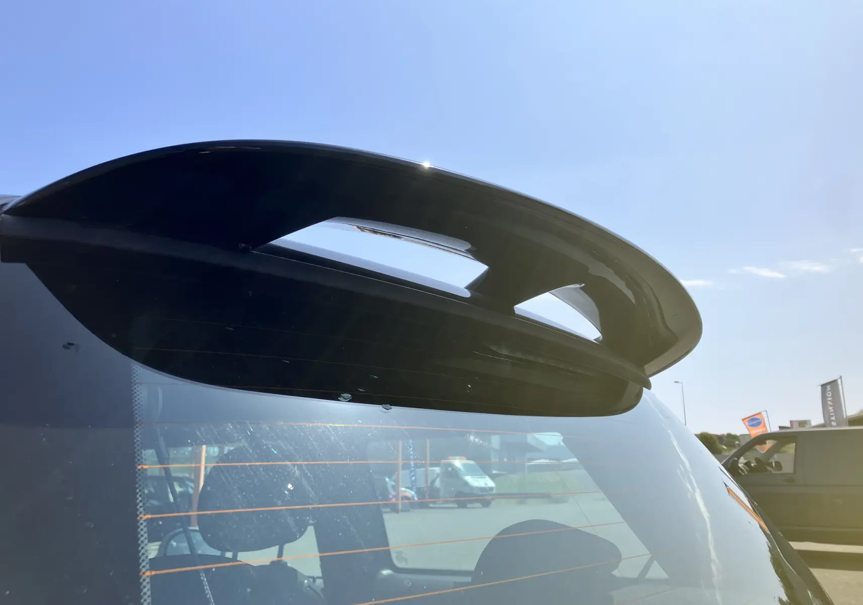 Gros plan sur l'aileron arrière noir d'une MINI Cooper S R56 marron, vue depuis l'arrière sous un ciel bleu.