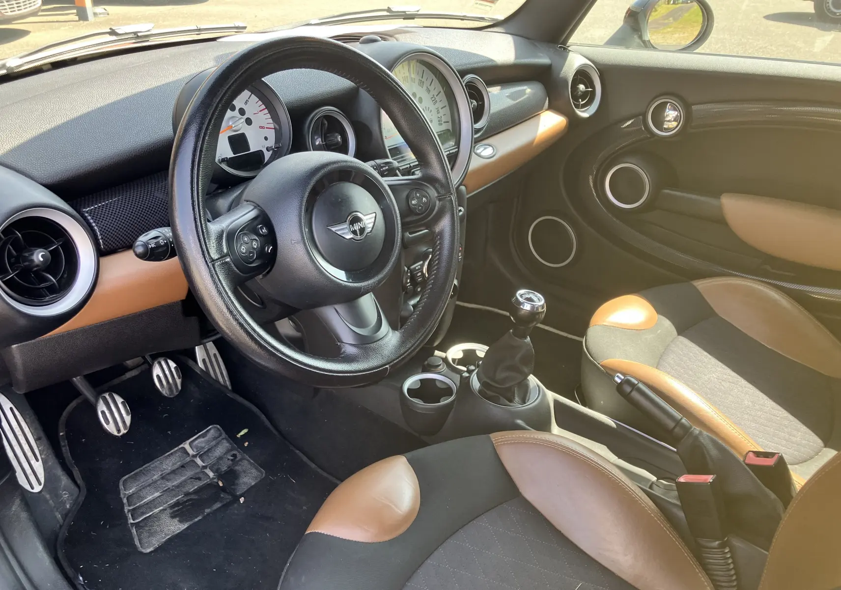 Intérieur de MINI Cooper S R56 2012 vue côté conducteur, volant cuir noir et sièges bi-ton marron et noir.