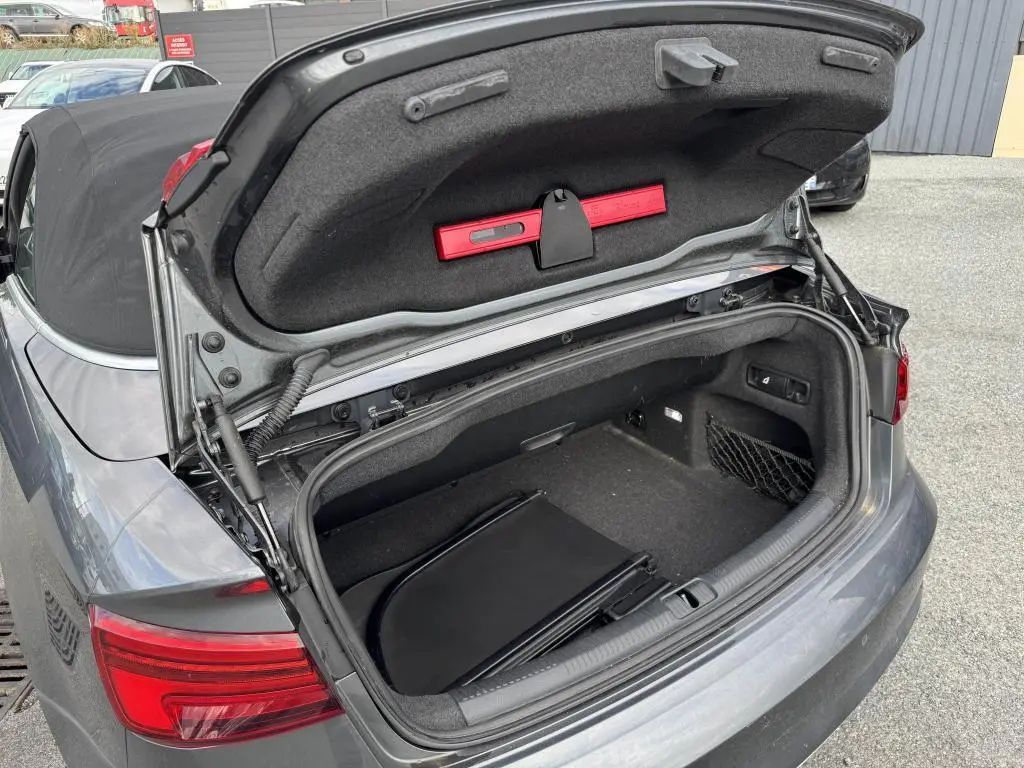 Coffre ouvert vu de l'arrière d'une Audi A3 Cabriolet gris avec capote noire et rangement intérieur visible.
