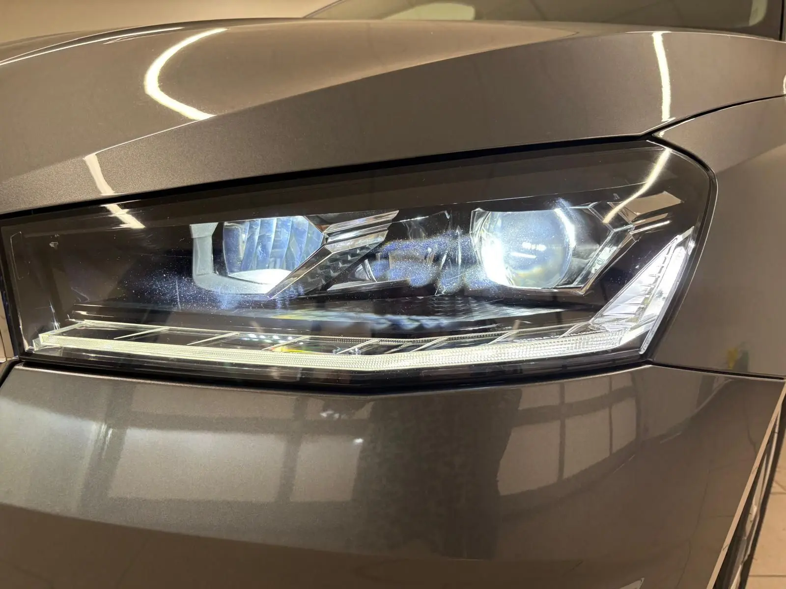 Gros plan sur le phare avant droit de la Skoda Fabia 2023 en peinture métallisée gris graphite, éclairage LED allumé.