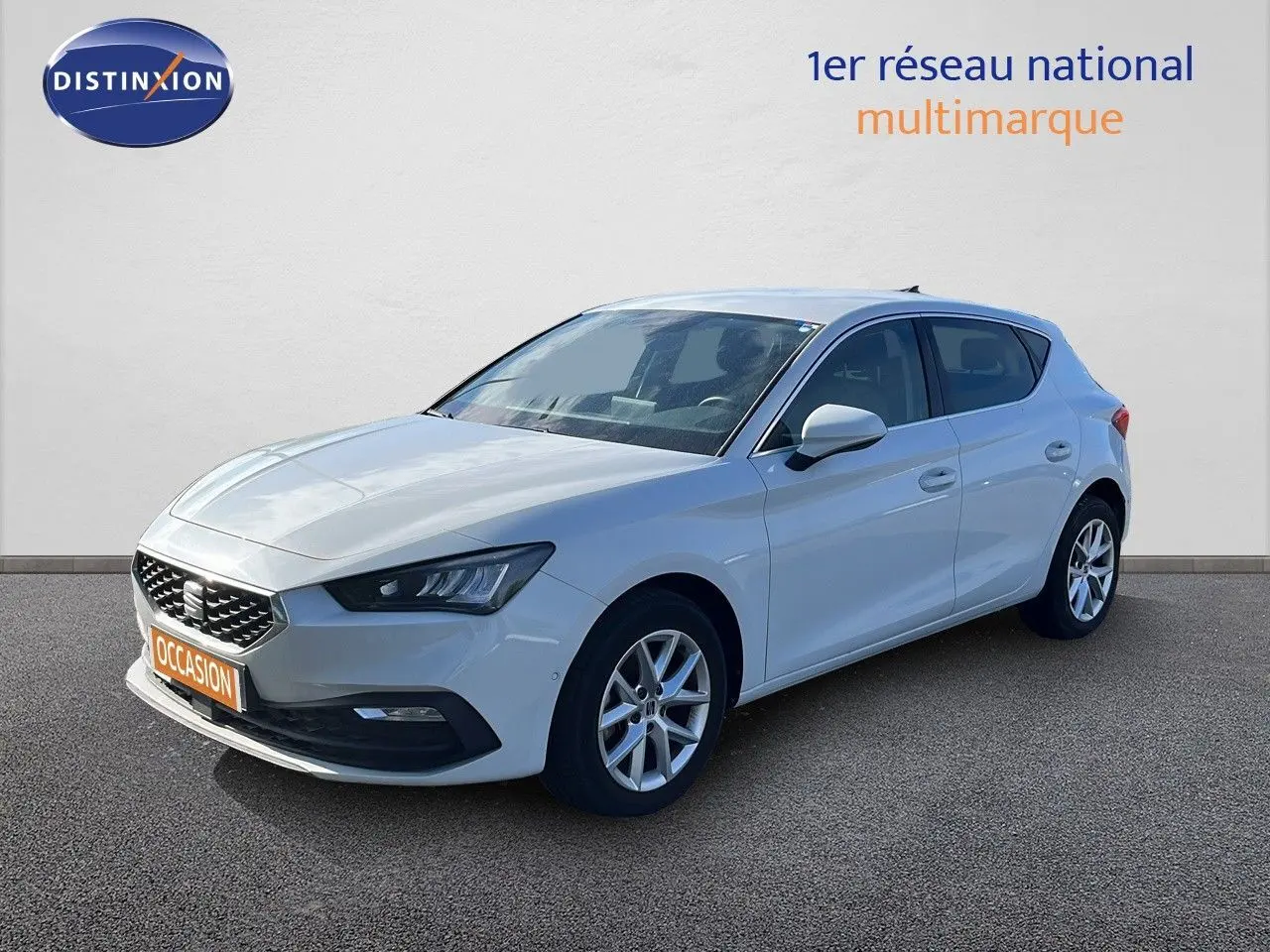 SEAT Leon blanc neige vue 3/4 avant droit, avec jantes alliage et calandre distinctive, stationnée sur sol gris.