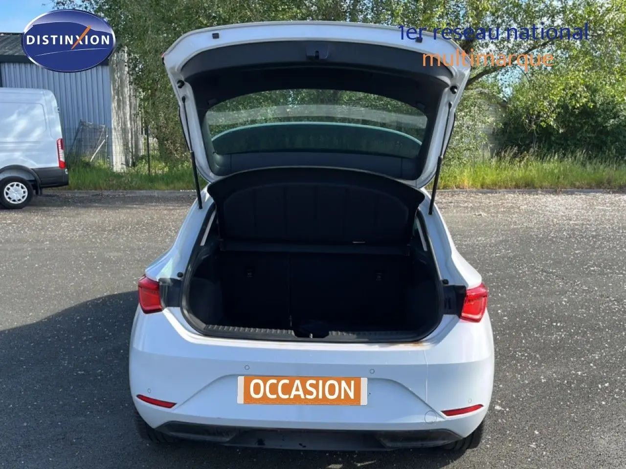 Vue arrière d'une SEAT LEON blanc neige 2025 avec le coffre ouvert sur un parking extérieur.