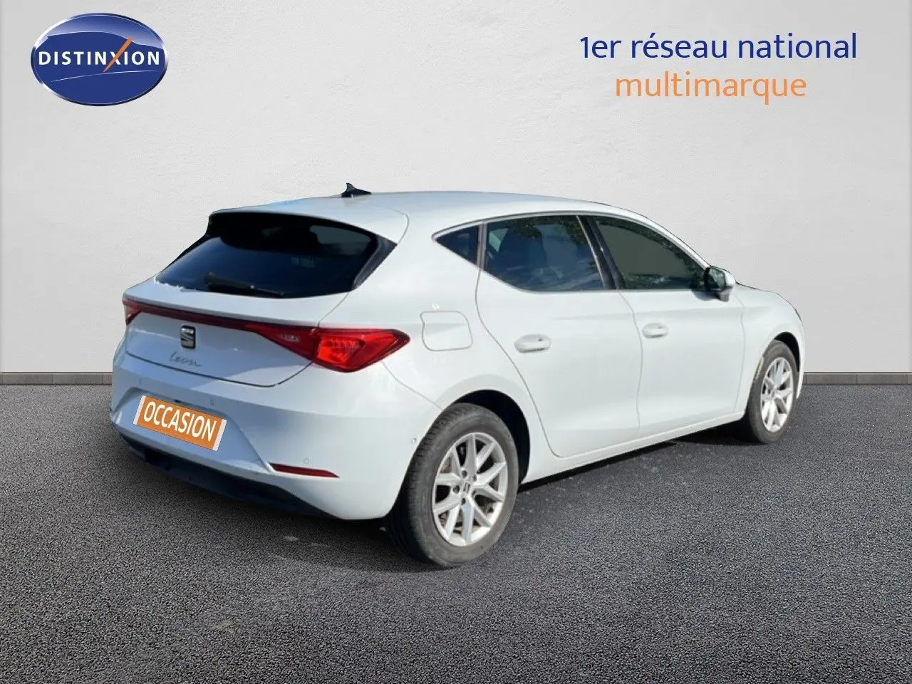 Vue 3/4 arrière droite d'une SEAT Leon blanche neige avec feux arrière LED et jantes alliage, stationnée sur sol gris.