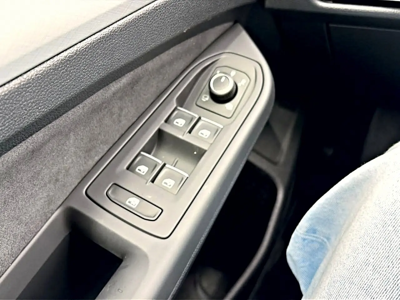 Vue rapprochée du panneau de commandes des vitres côté conducteur d’une Volkswagen Golf noire, avec boutons de réglage des rétroviseurs.