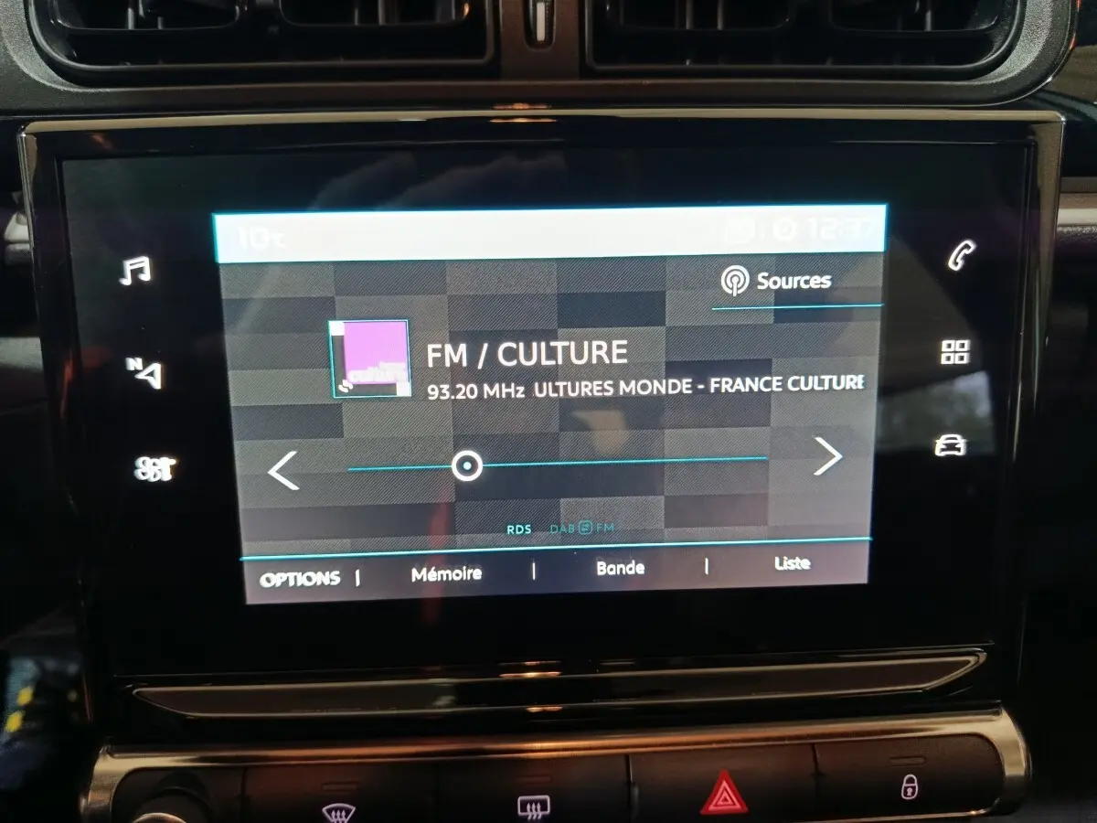 Écran tactile central de la Citroën C3 gris clair 2024 affichant une station FM sur fond noir brillant.
