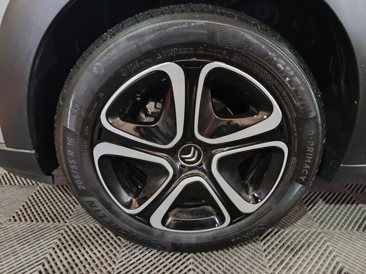 Gros plan sur la roue avant droite d'une Citroën C3 gris clair 2024 avec jante alliage noire et argentée distinctive.