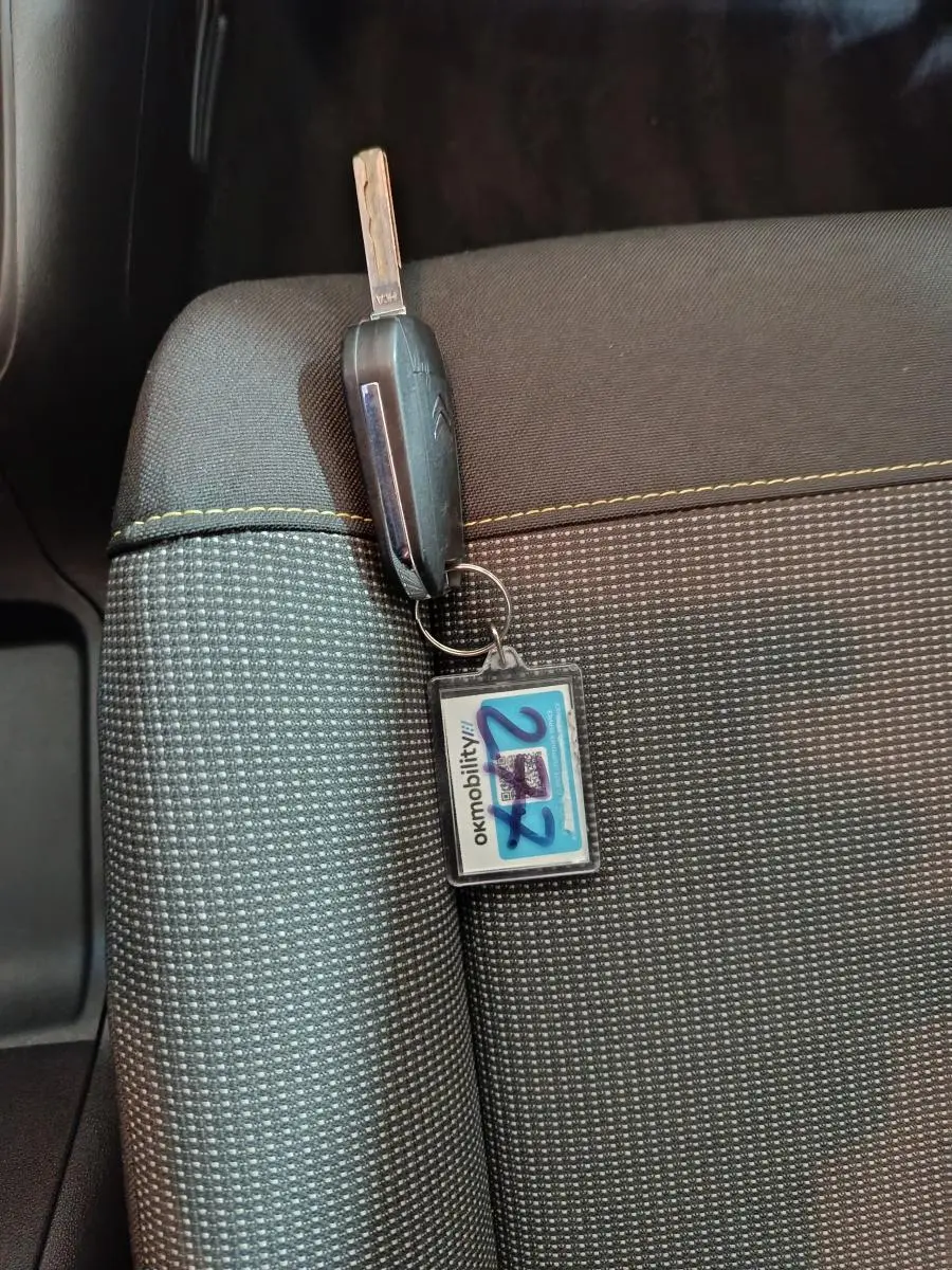 Gros plan sur une clé Citroën posée sur un siège tissu gris clair avec surpiqûres jaunes.