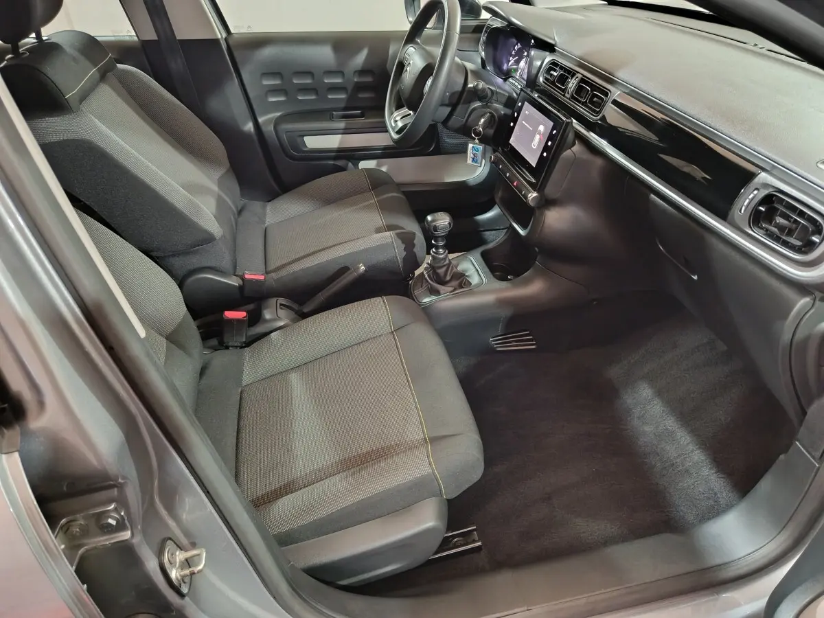 Vue intérieure côté conducteur de la Citroën C3 gris clair 2024, avec sièges tissu, volant multifonctions et écran tactile central.