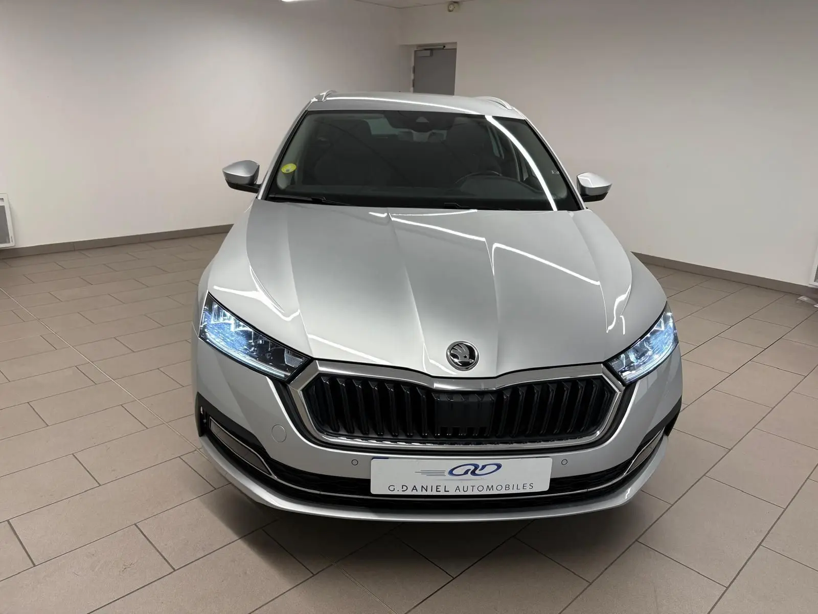 Vue avant d'une Skoda Octavia Combi gris argent 2023 avec phares LED allumés et calandre noire brillante.