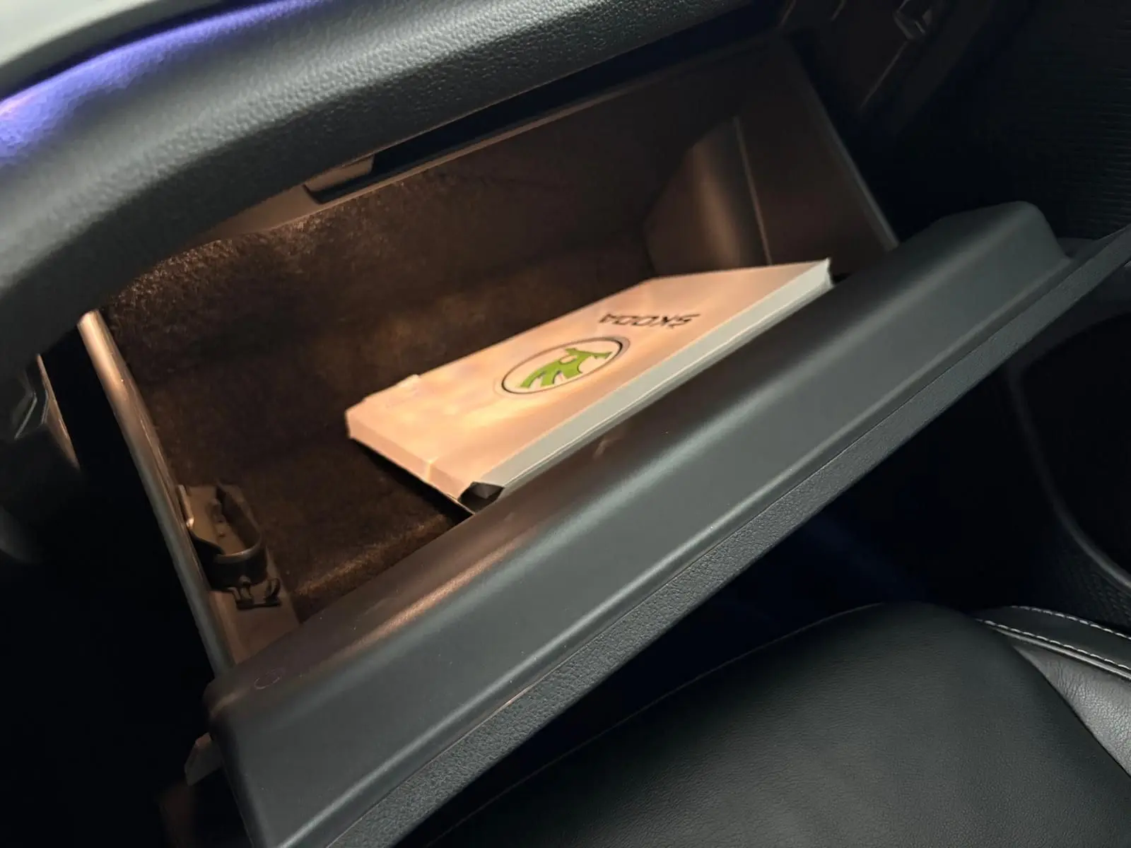 Boîte à gants ouverte côté passager d'une Skoda Octavia Combi gris argent 2023 avec manuel visible à l'intérieur.