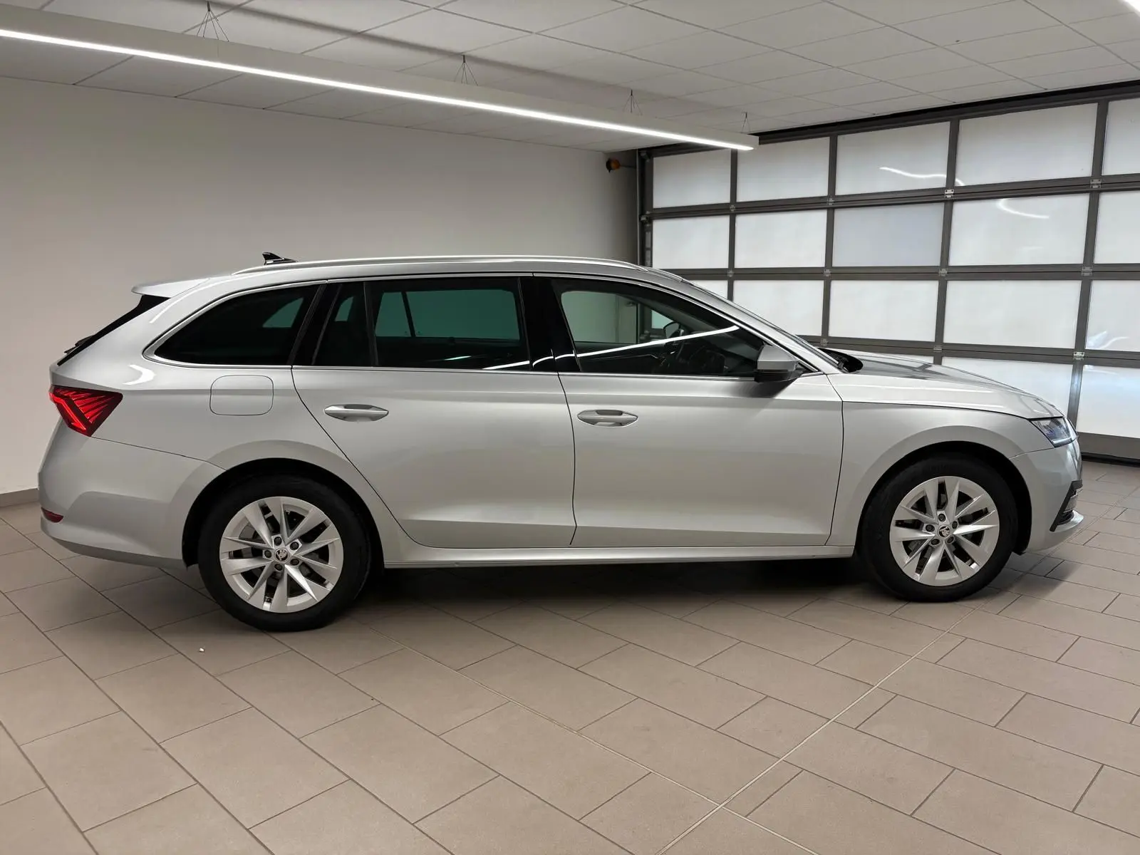 Skoda Octavia Combi 2023 gris argent vue de profil côté gauche dans un garage lumineux avec jantes alliage.