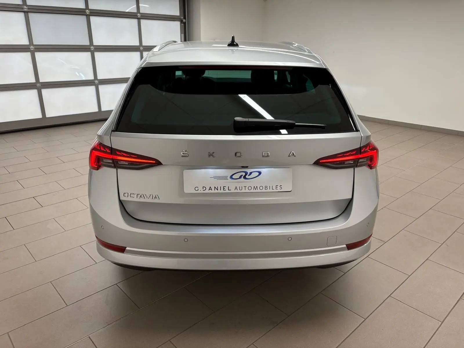 Vue arrière d'un Skoda Octavia Combi gris argent 2023 avec feux LED allumés dans un showroom.