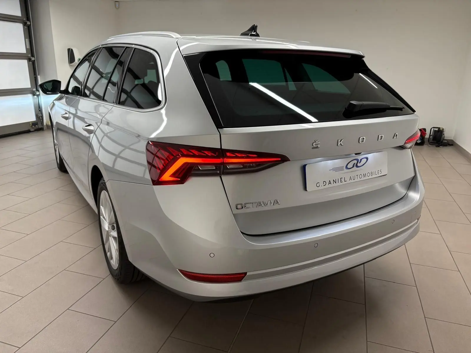 Vue 3/4 arrière droite d'une Skoda Octavia Combi gris argent 2023 avec feux arrière LED allumés en intérieur showroom.