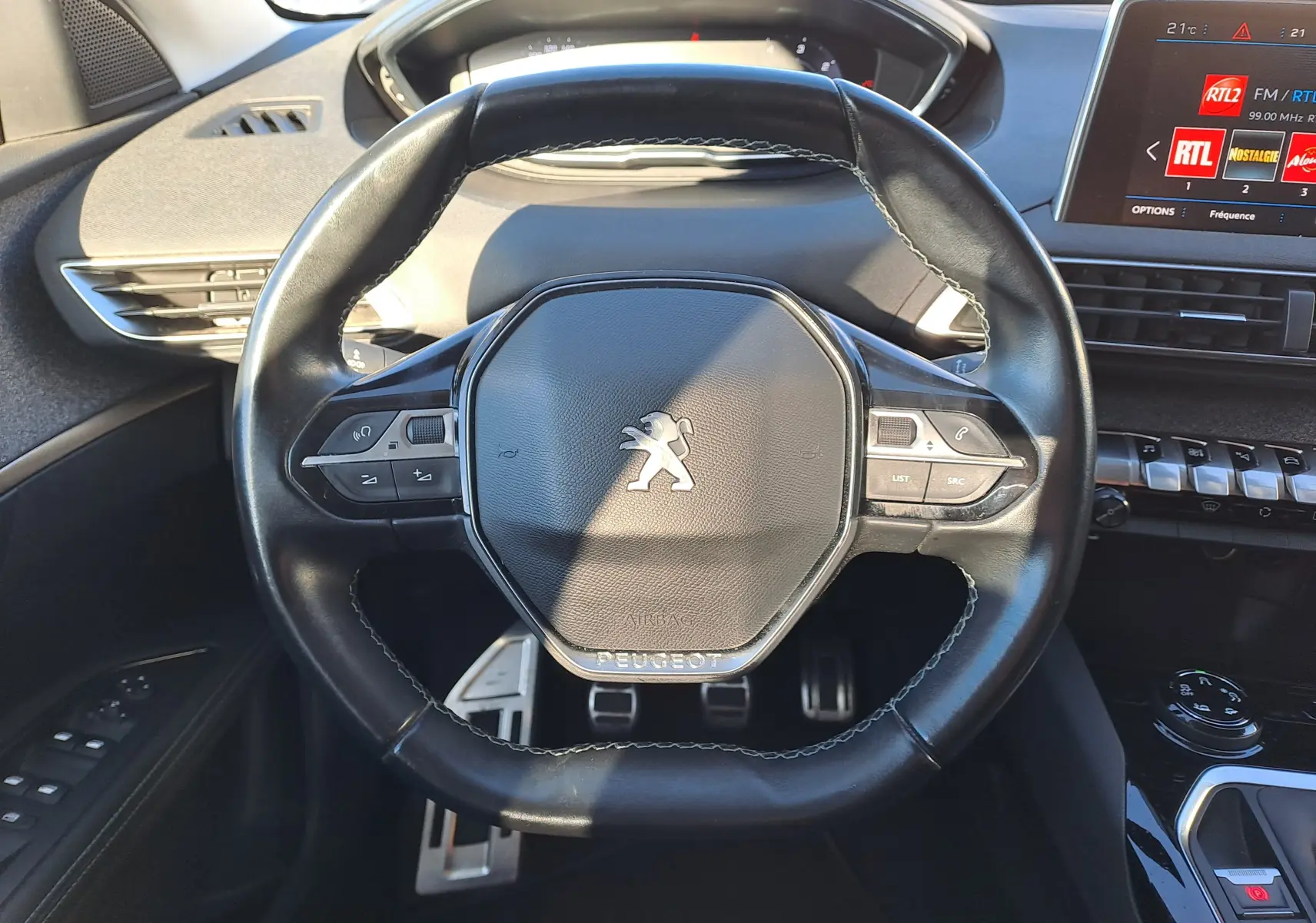 Vue rapprochée du volant noir en cuir du Peugeot 5008 gris, avec tableau de bord et écran tactile affichant la radio RTL.
