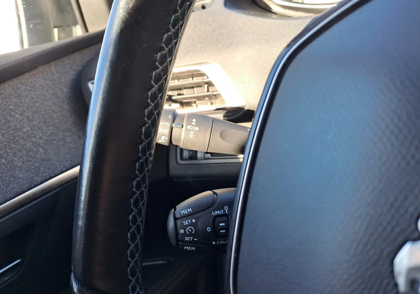 Gros plan sur le volant en cuir noir et les commandes de régulateur de vitesse du Peugeot 5008 gris, intérieur côté gauche.