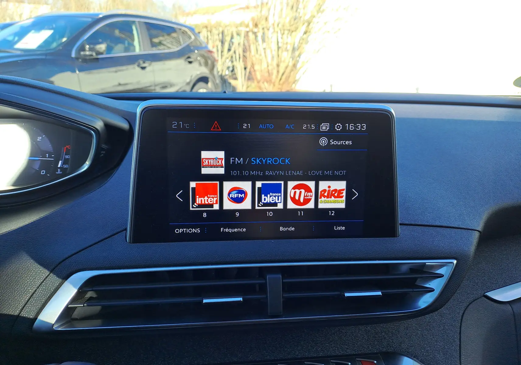 Vue intérieure du tableau de bord du Peugeot 5008 gris, avec écran tactile central affichant les stations radio FM.