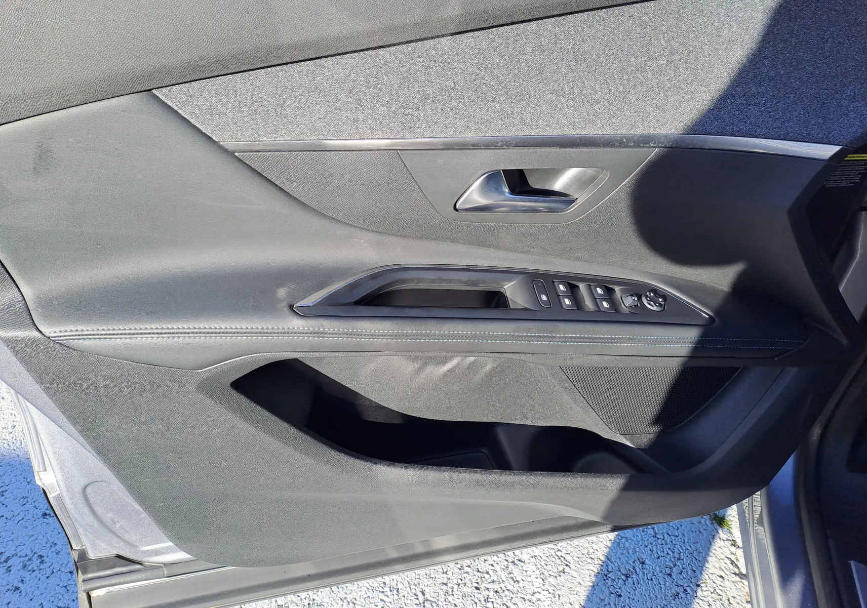 Vue intérieure côté gauche de la porte avant grise du Peugeot 5008 avec commandes des vitres et poignée argentée.