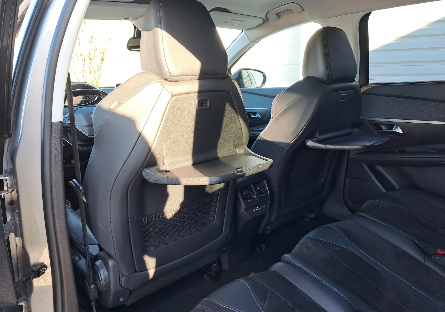 Vue intérieure arrière du Peugeot 5008 gris 2019 montrant les dossiers avec tablettes pliantes et sièges en cuir noir.