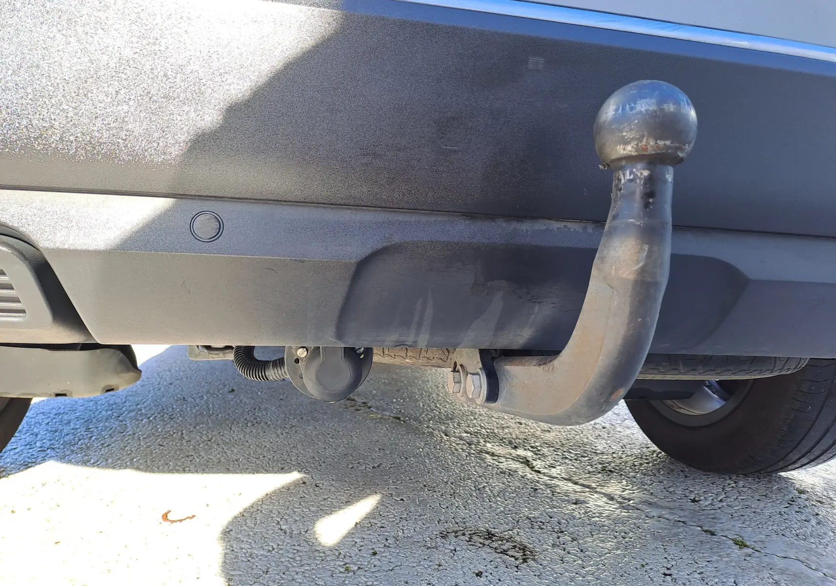 Gros plan sur l'attelage arrière en métal d'un Peugeot 5008 gris, avec la roue arrière droite partiellement visible.