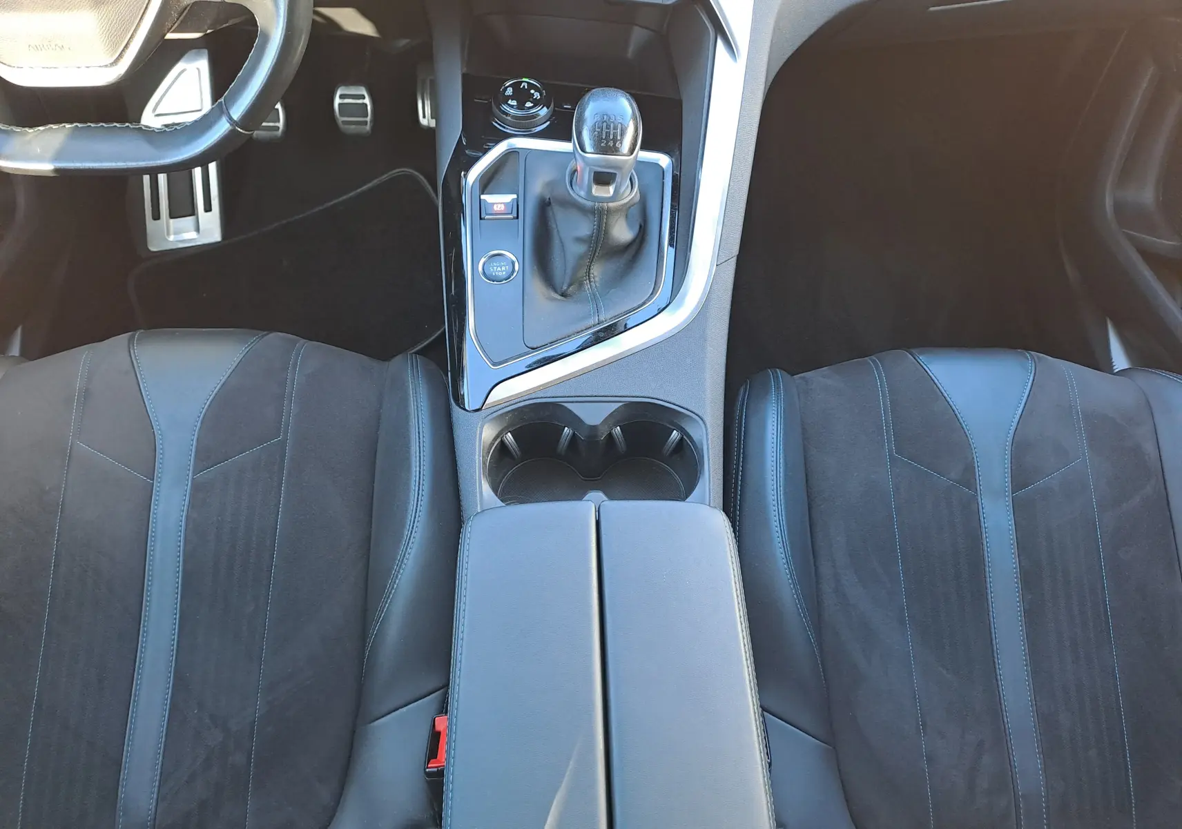 Vue intérieure centrée sur la console centrale et les sièges avant en cuir noir du Peugeot 5008 gris, boîte manuelle.