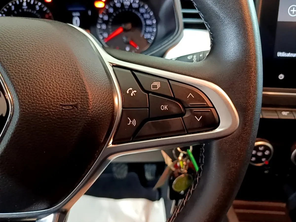 Gros plan sur les commandes multifonctions à droite du volant cuir noir de la Renault Clio Business TCe 100 GPL blanche, tableau de bord en arrière-plan.