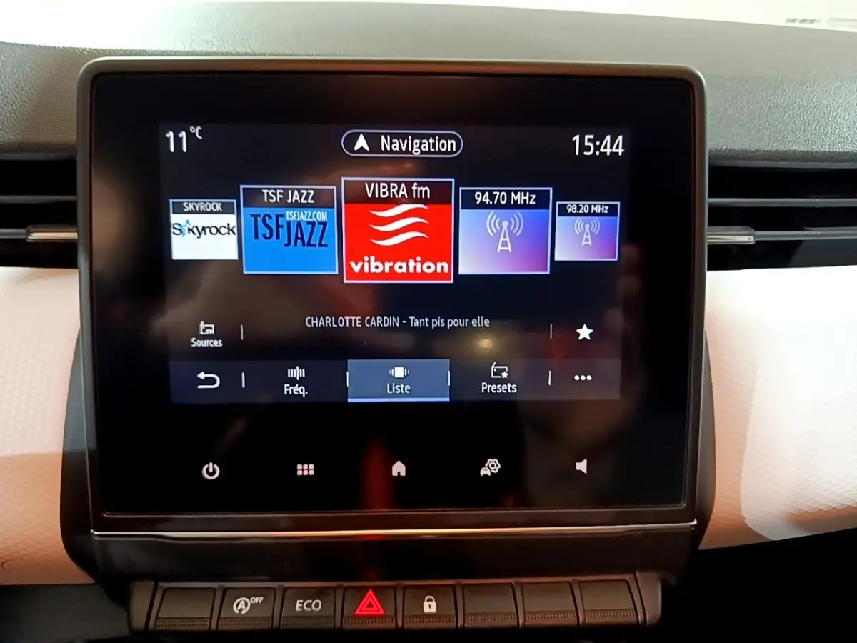 Écran tactile central affichant la radio et la navigation dans l'habitacle clair d'une Renault Clio blanche 2023.