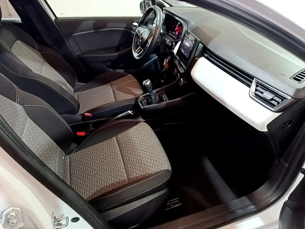 Vue intérieure côté conducteur de la Renault Clio Business blanche, montrant sièges, volant cuir et tableau de bord moderne.