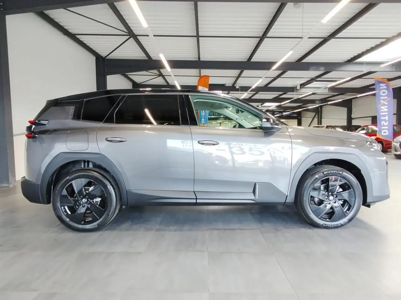 Profil côté gauche du Citroën C5 Aircross gris métallisé avec toit noir et jantes alliage noires en intérieur showroom.