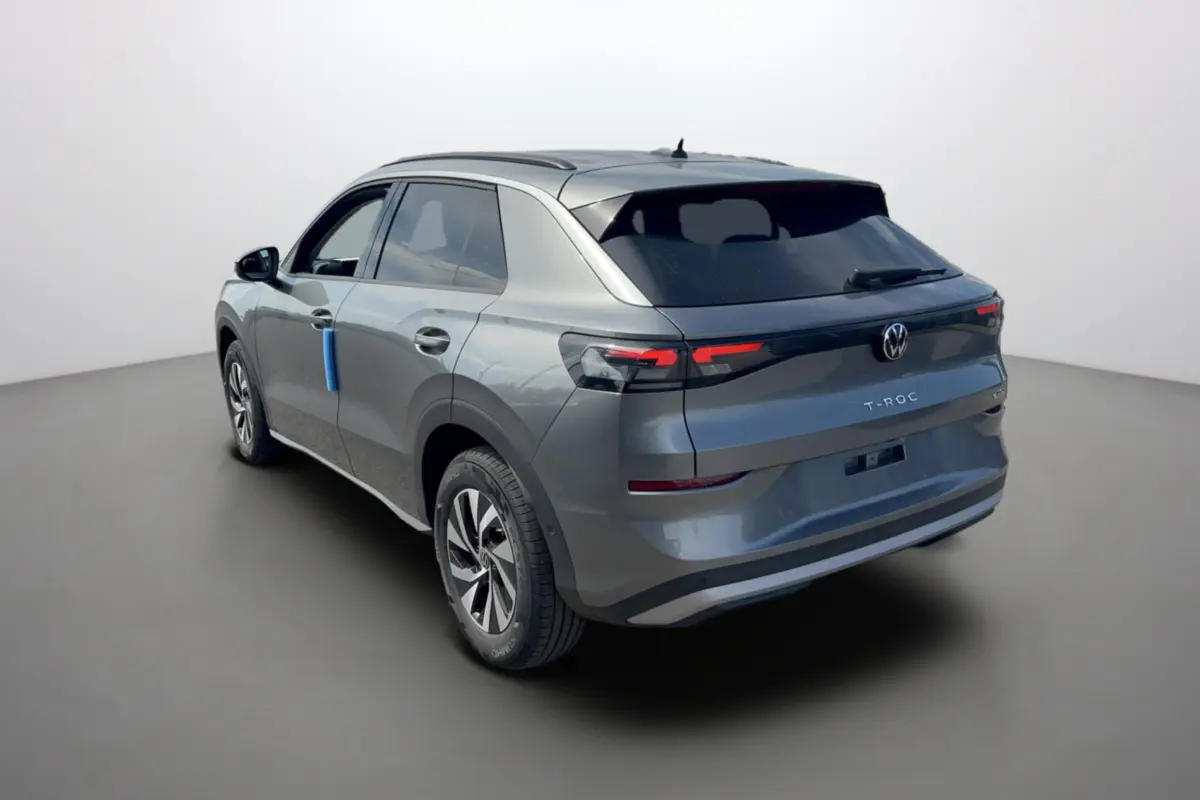 Vue 3/4 arrière gauche d'un Volkswagen T-Roc gris loup 2026 avec feux arrière LED et jantes alu 16 pouces.