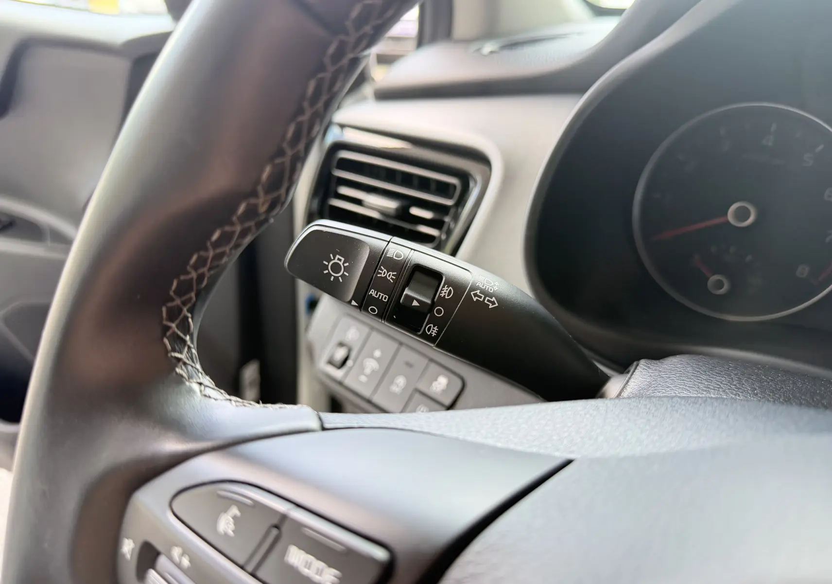 Gros plan sur le commodo des phares et clignotants côté gauche du volant d’un Kia Stonic blanc, intérieur noir.