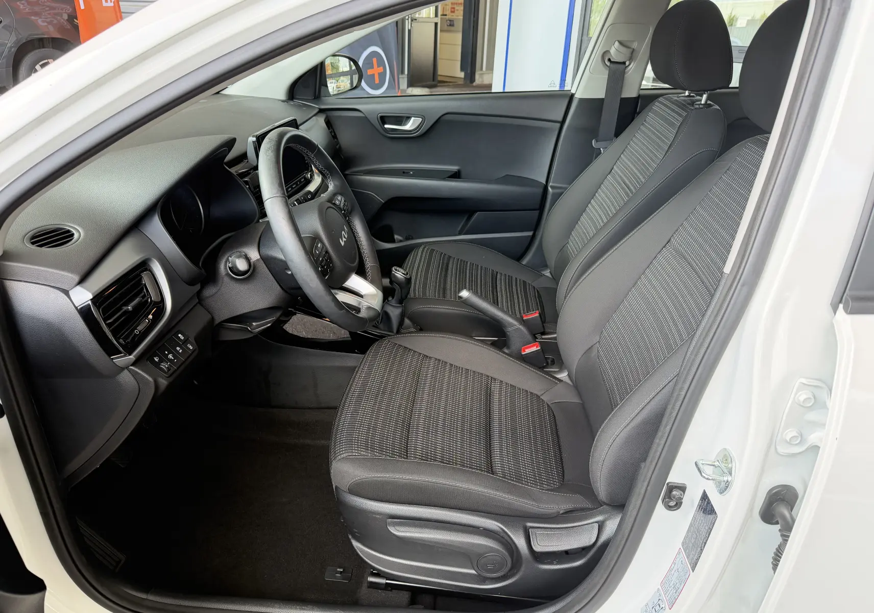 Vue intérieure côté conducteur du Kia Stonic blanc 2022, montrant sièges tissu noirs et tableau de bord moderne.