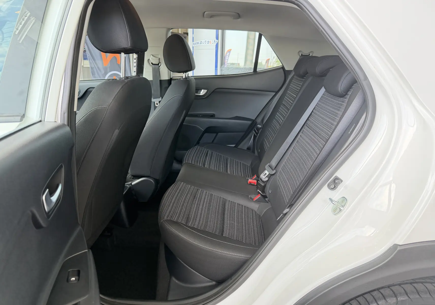 Vue intérieure côté arrière droit du Kia Stonic blanc 2022, montrant les sièges arrière en tissu noir avec motifs rayés.