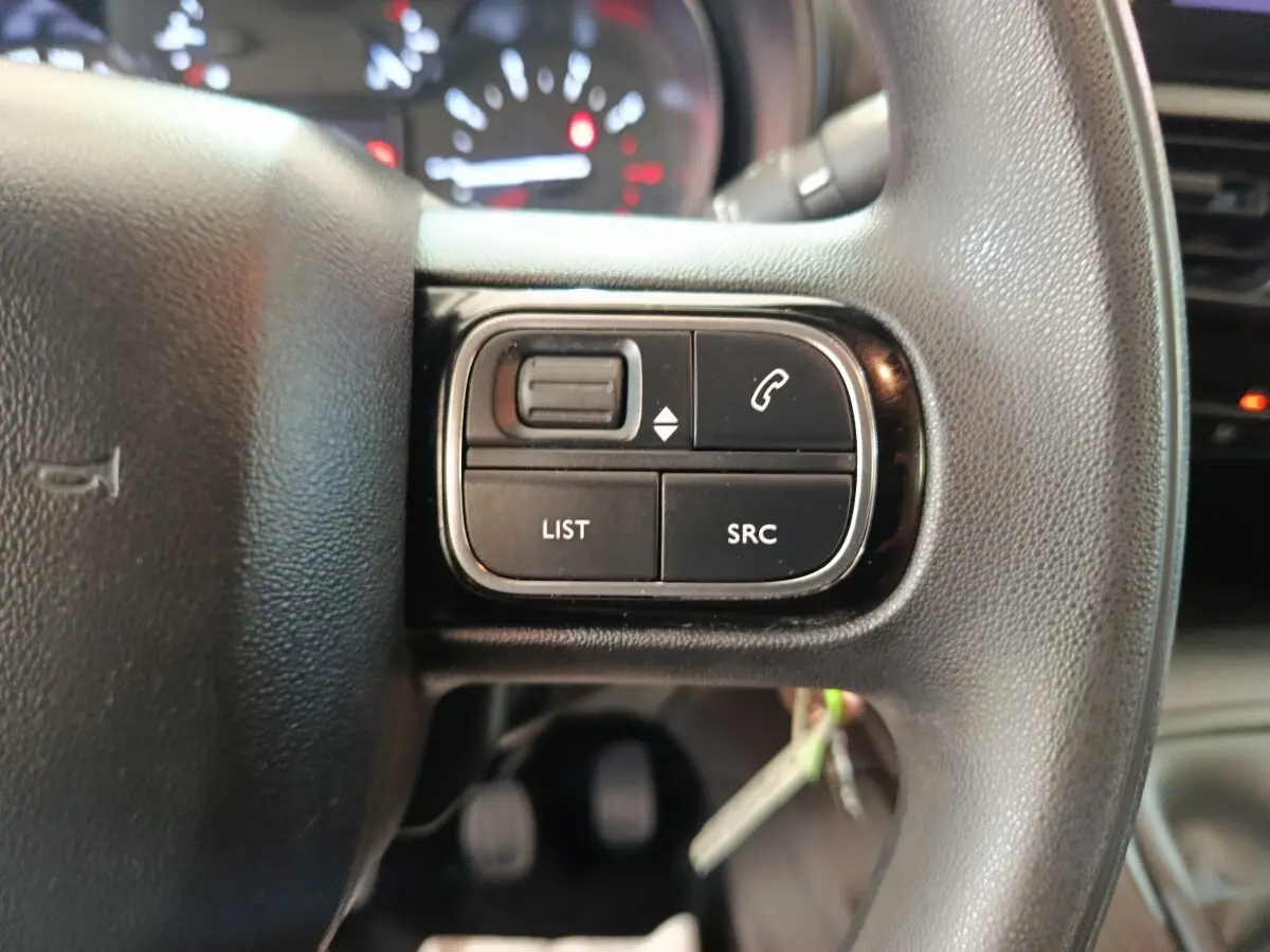 Gros plan sur les commandes gauche du volant noir du Citroën Berlingo blanc, avec tableau de bord flou en arrière-plan.
