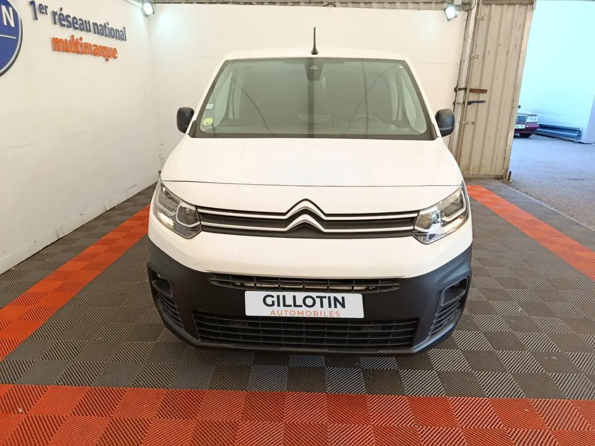 Vue de face d’un Citroën Berlingo blanc avec pare-chocs noir et phares allumés dans un garage.
