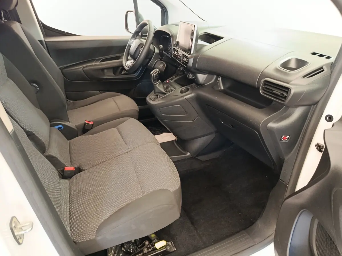 Vue intérieure côté conducteur du Citroën Berlingo blanc 2020, montrant sièges tissu gris et tableau de bord noir.