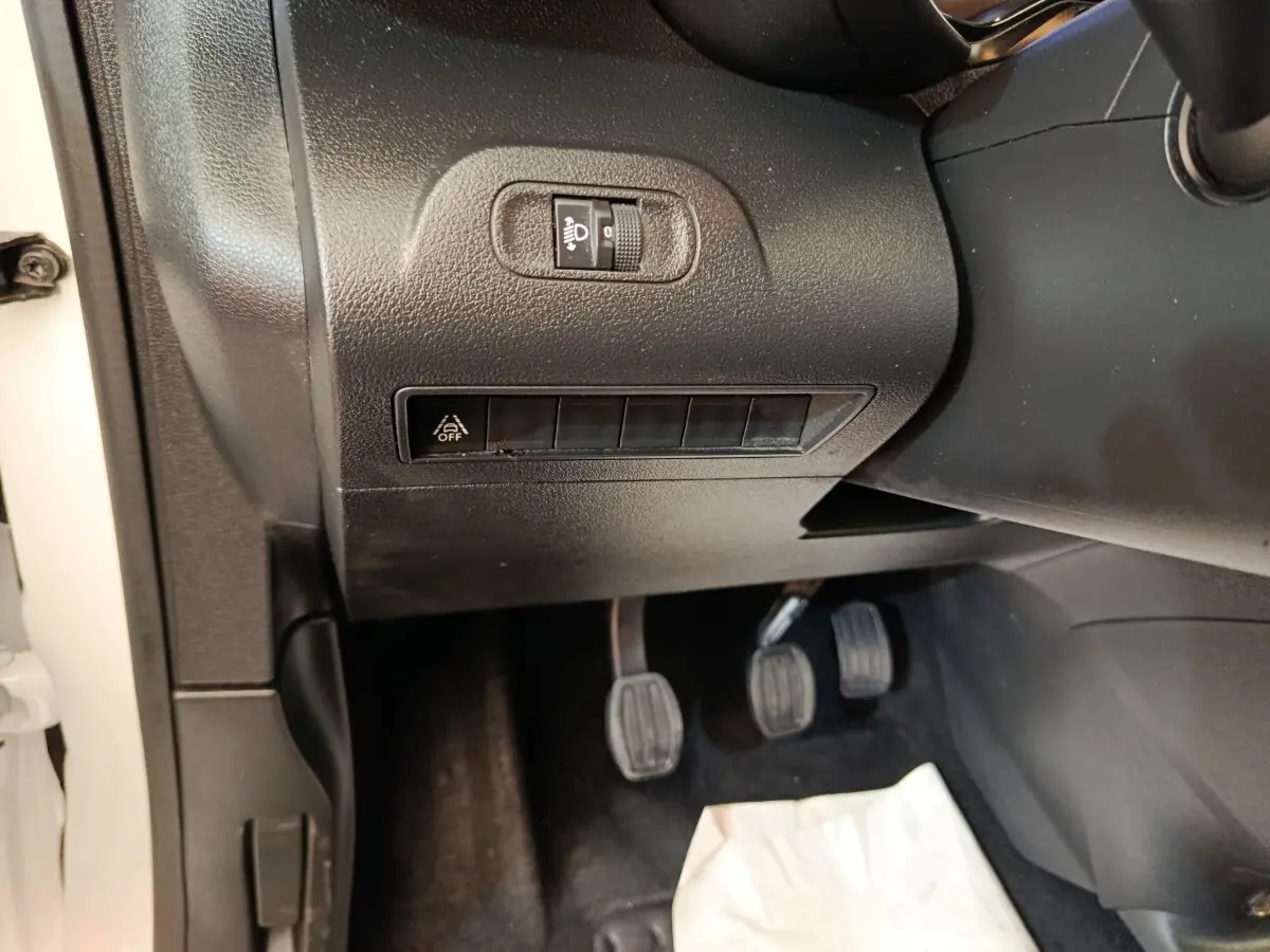 Détail intérieur côté conducteur du Citroën Berlingo blanc 2020 montrant les pédales et commandes de réglage des phares.