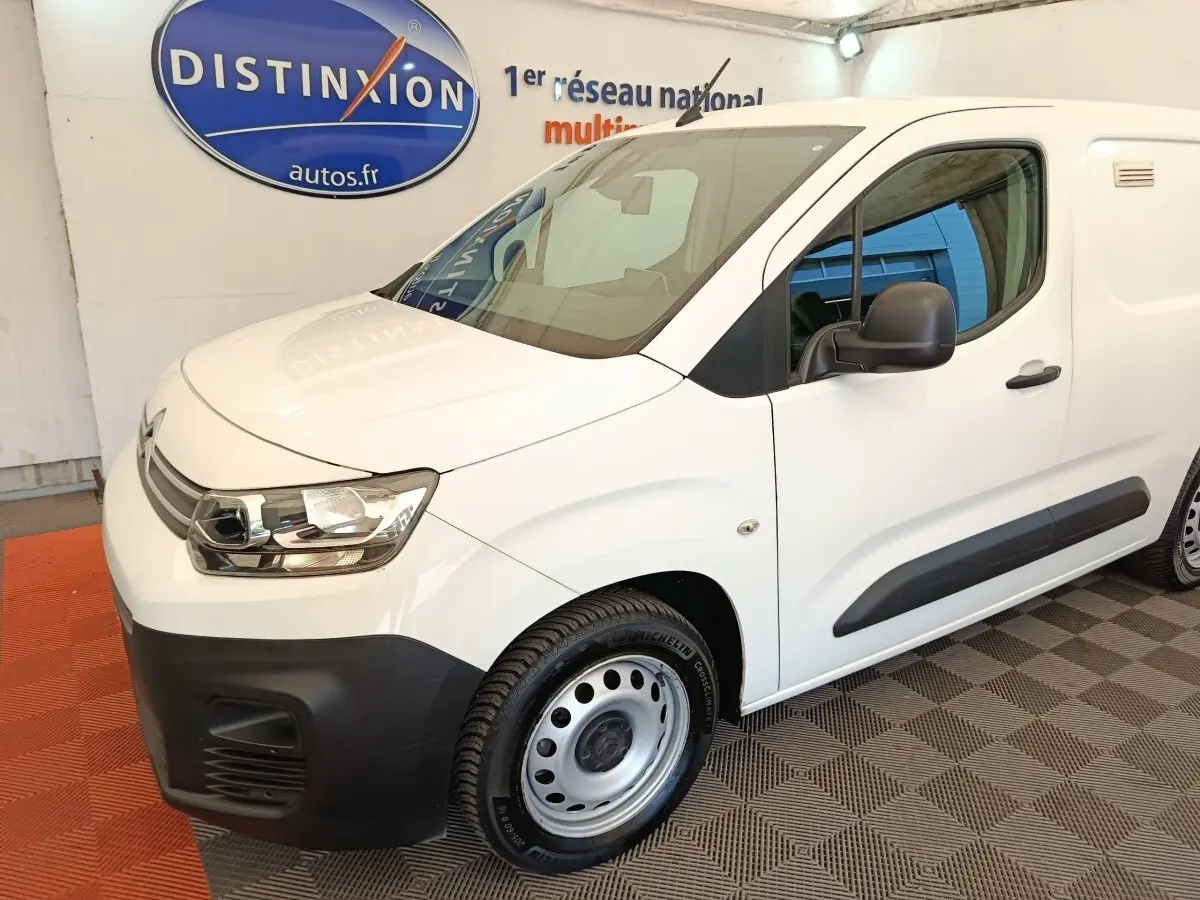 Vue 3/4 avant droit d’un Citroën Berlingo blanc utilitaire avec pare-chocs noir et jantes acier en showroom.