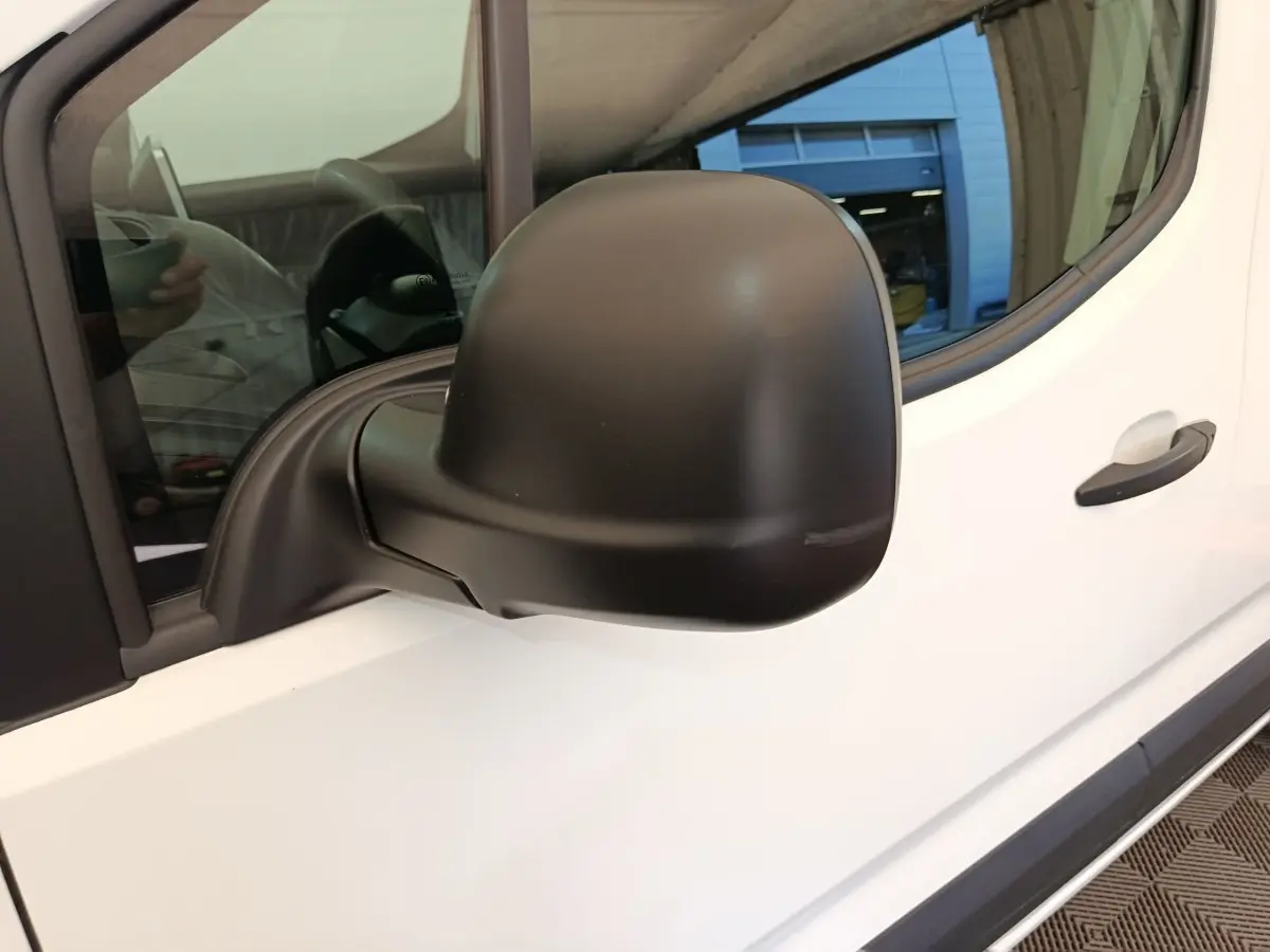Rétroviseur noir côté conducteur d’un Citroën Berlingo blanc, vue rapprochée sur la portière avant gauche.