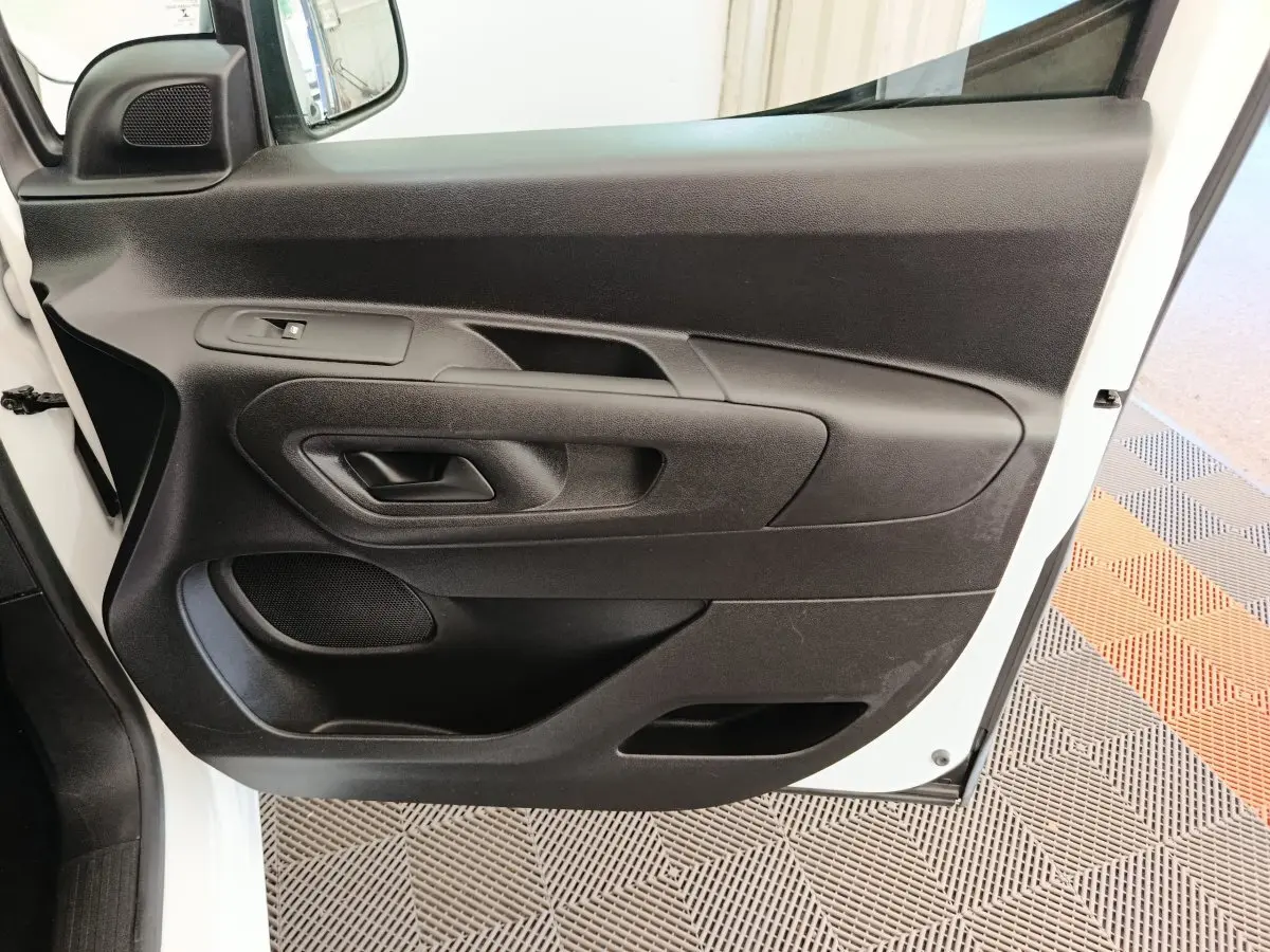 Vue rapprochée de la porte avant gauche noire du Citroën Berlingo blanc, montrant la poignée et la commande de vitre.