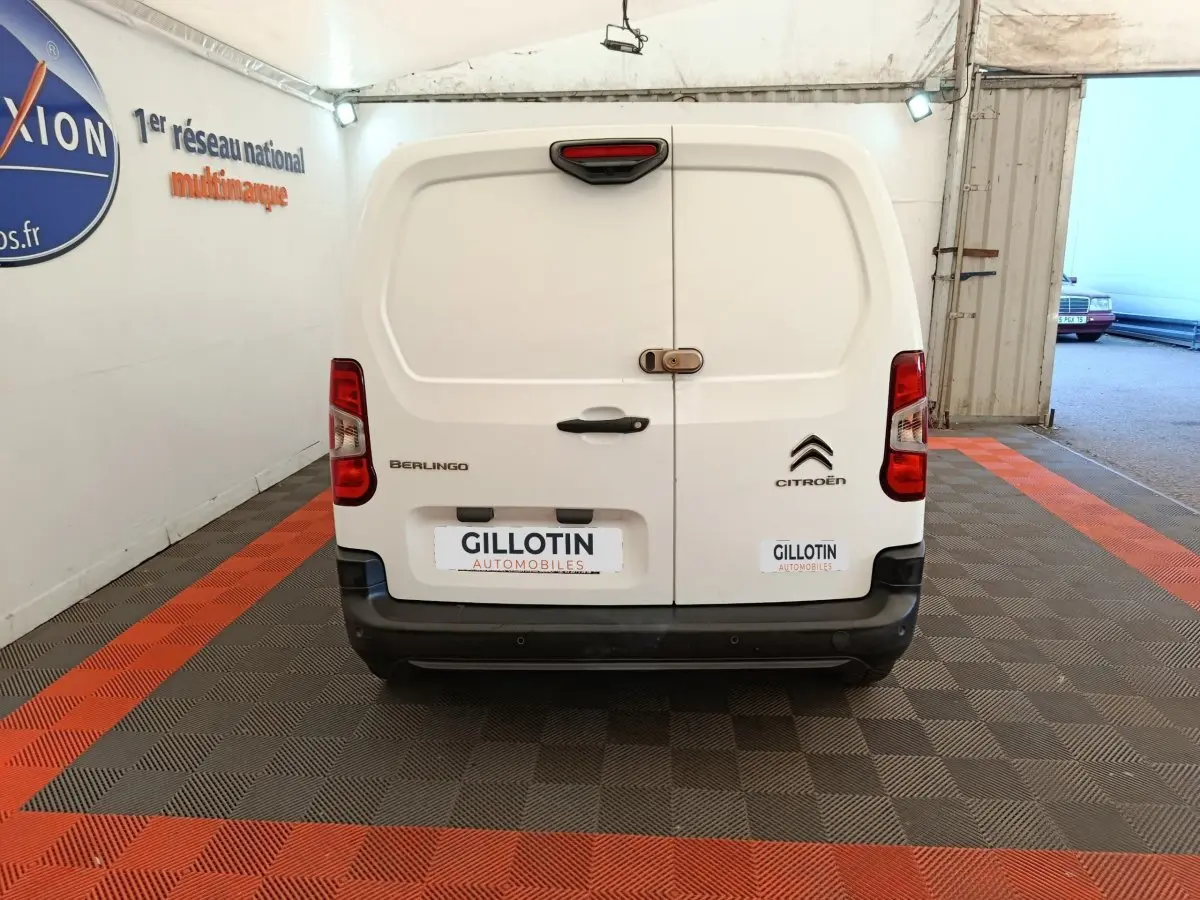 Vue arrière d'un utilitaire Citroën Berlingo blanc avec portes battantes et feux arrière rouges, stationné en intérieur.
