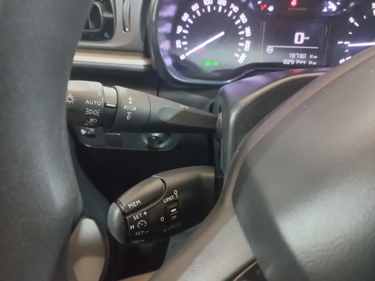 Gros plan sur le volant noir et les commandes de régulateur de vitesse de la Citroën C3 2024, tableau de bord en arrière-plan.