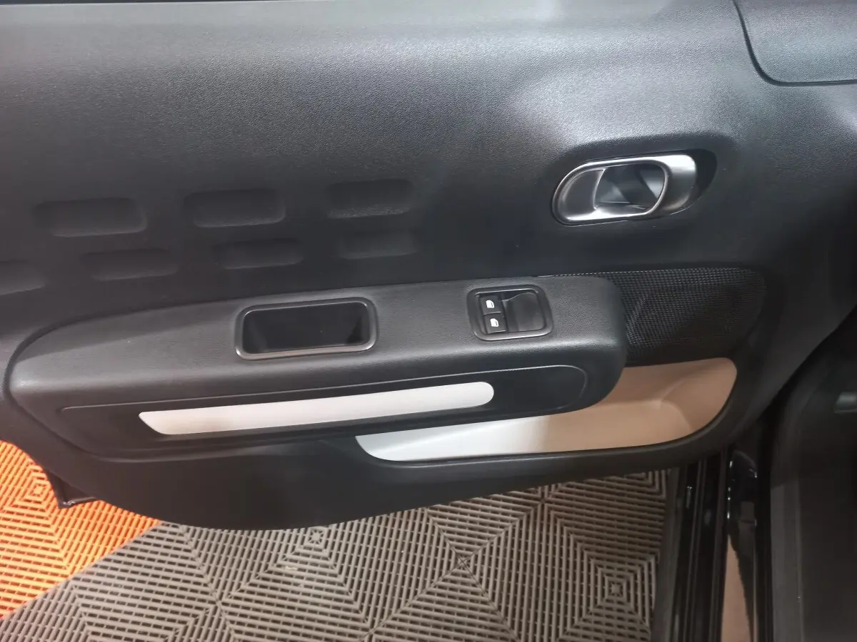 Vue intérieure de la porte côté conducteur de la Citroën C3 noire, avec commandes de vitres et poignée argentée.